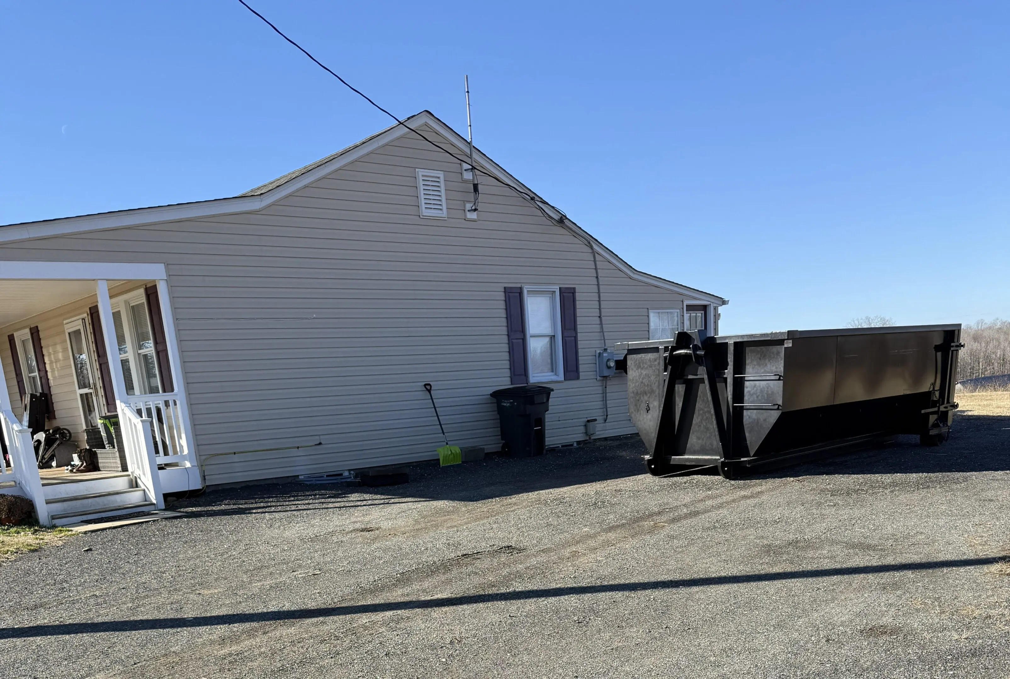Side view of a beige house with trash bins and outdoor equipment on a sunny day.